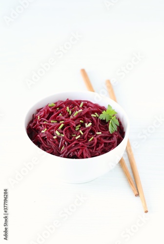 Korean beetroot salad with garlic and parsley in a bowl with wooden sticks on a white background