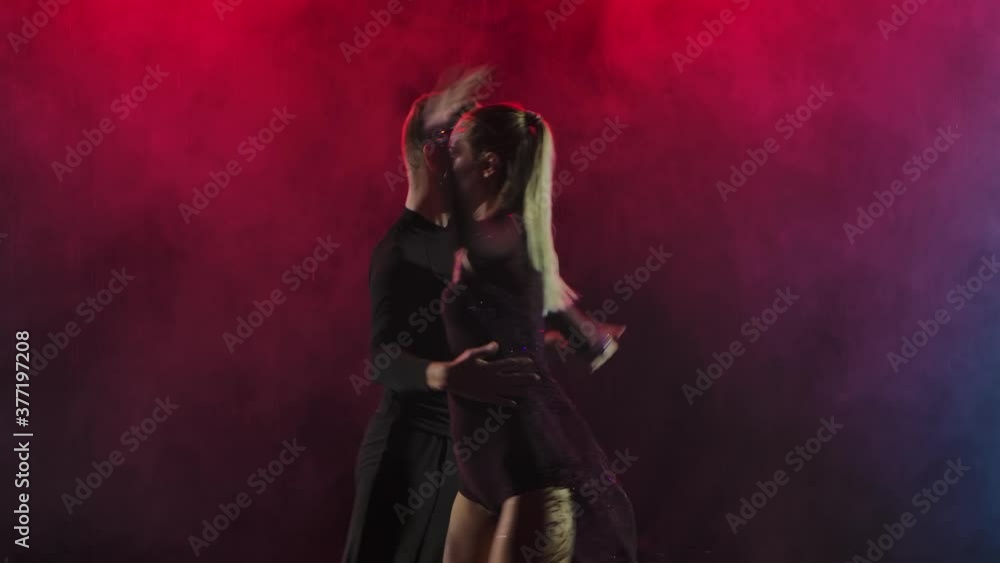 Young couple cheerfully dancing jive on a smoky background with crimson backlight. Slow motion. Close up. Young couple cheerfully dancing jive on a smoky background with crimson backlight. Slow motion. Close up.