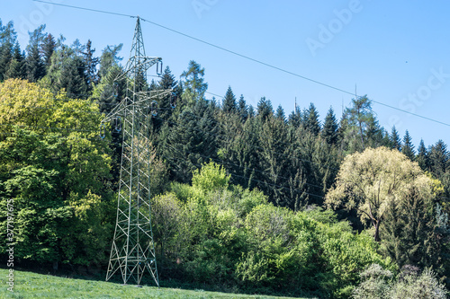 Power pylon on the green field near the forest