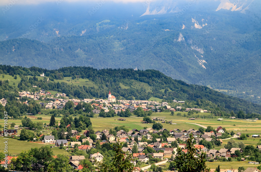 Panoramic landscape in Slovenia countryside in a sunny summer day. The meadow, fields and green mountains, the village at the foot of the mountain. Travel Slovenia.