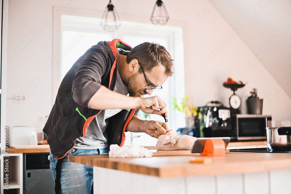 attractive nerd guy with glasses in stylish kitchen follows a recipe on the phone prepares chicken attractive nerd guy with glasses in stylish kitchen follows a recipe on the phone prepares chicken