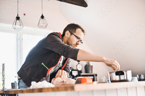 attractive nerd guy with glasses in stylish kitchen follows a recipe on the phone prepares chicken