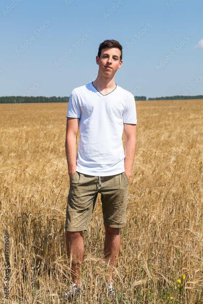 Handsome teen age fellow with hands in pockets standing on an agricultural field, full-length portrait Handsome teen age fellow with hands in pockets standing on an agricultural field, full-length portrait