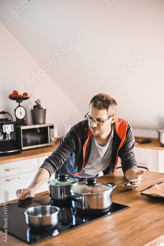 attractive nerd guy with glasses in stylish kitchen follows a recipe on the phone prepares chicken