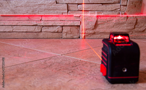 The red light beams of the laser level device on the wall and floor show the direction. copyspace for text.