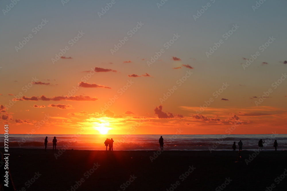 persone che ammirano il tramonto in riva al mare