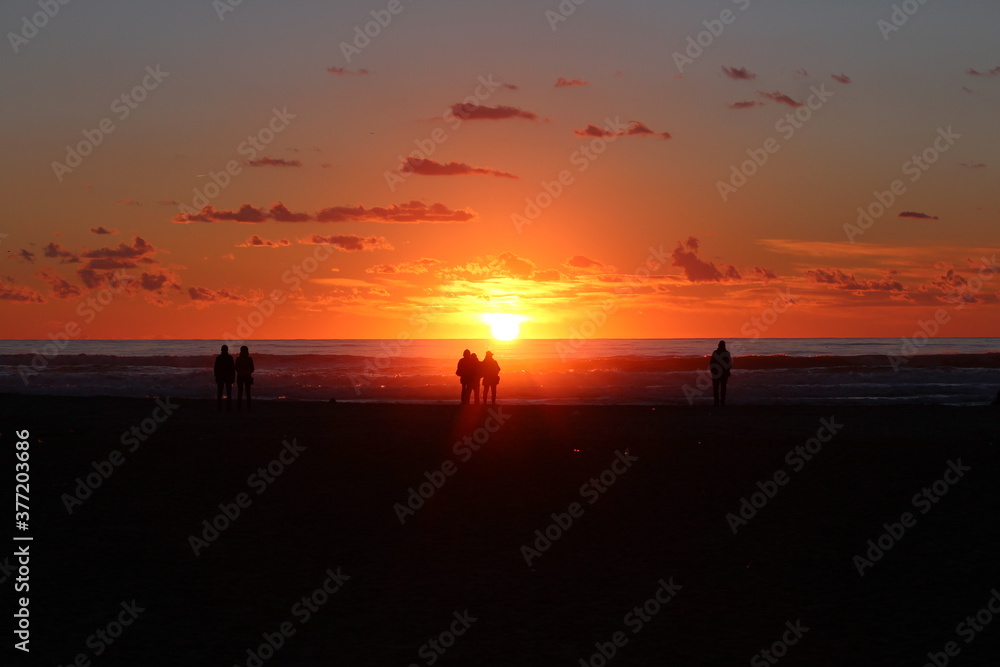 persone che ammirano il tramonto in riva al mare