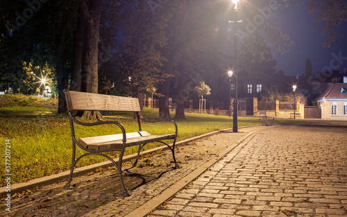 Wooden Bench in a City Park Illuminated by a Street Lamp, Inviting Night Calm Mood
