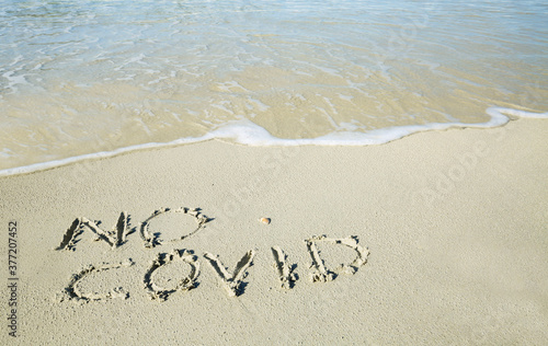 "No covid" written on the sand of the shore of a beach with incoming waves. Fear of beach resort managers for the upcoming summer season due to the coronavirus covid-19