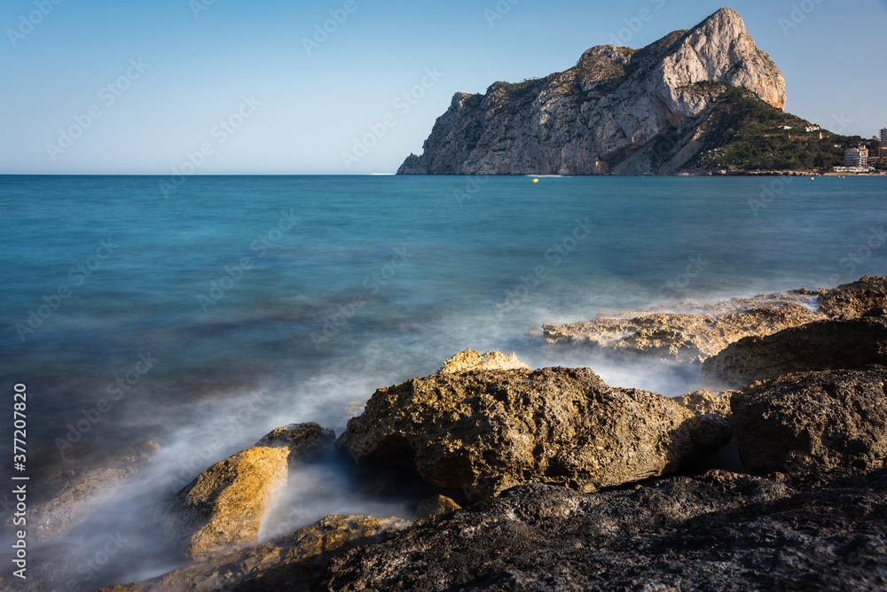 Sea foam from waves breaking against the rocky coastline with Calpe crag in the background, Alicante, Spain