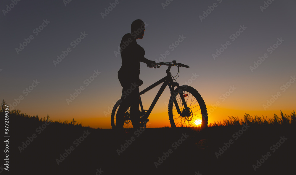 Silhouette of a man standing with mountain bike at sunset