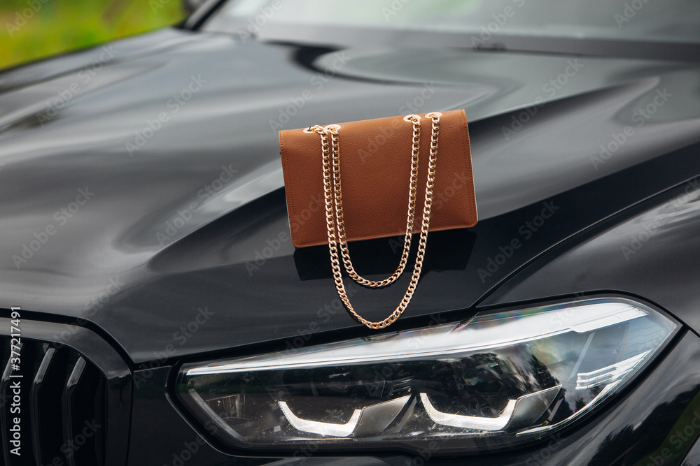 Women's handbag at the hood of a luxury car