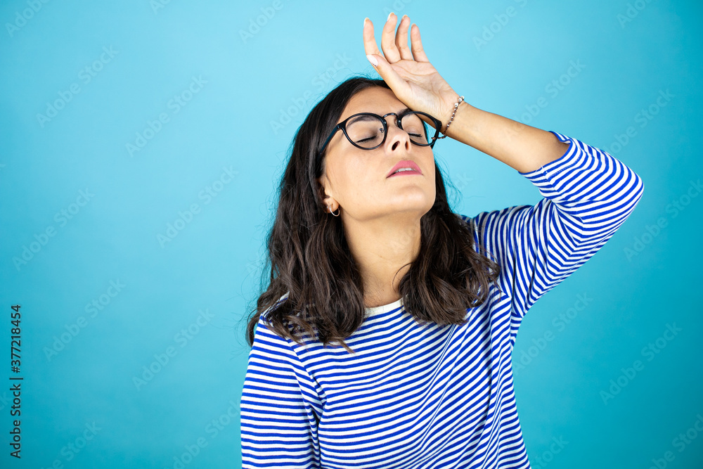 Pretty woman wearing glasses standing over insolated blue background suffering from headache desperate and stressed because pain and migraine with her hands on head very tired. Pretty woman wearing glasses standing over insolated blue background suffering from headache desperate and stressed because pain and migraine with her hands on head very tired.
