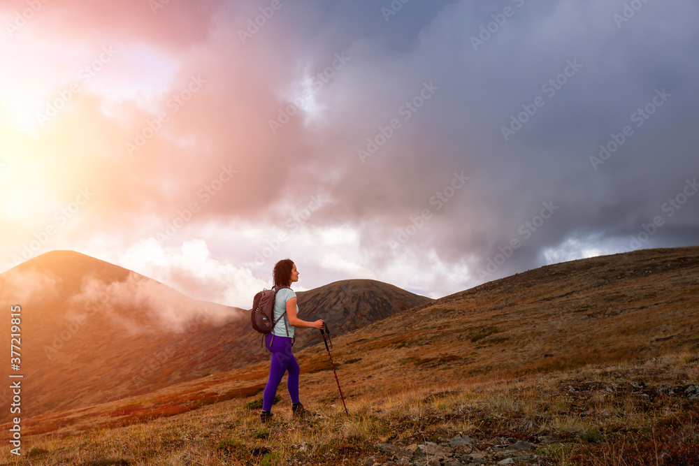 Adventurous Girl Hiking up the Nares Mountain during a cloudy and sunny sunset. Taken at Carcross, near Whitehorse, Yukon, Canada.