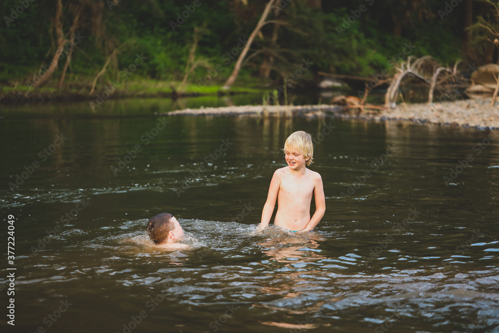 Fototapeta premium Two brothers swimming in river with strong current. Smiling while splashing in water.