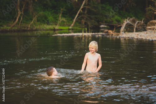 Two brothers swimming in river with strong current. Smiling while splashing in water.