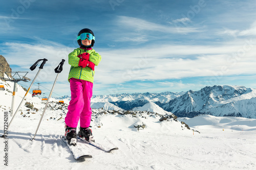 Active adorable preschooler caucasian kid girl portrait with ski in helmet, goggles and bright suit enjoy winter extreme sport activities. Little child skiing on luxury alpine resort in mountains