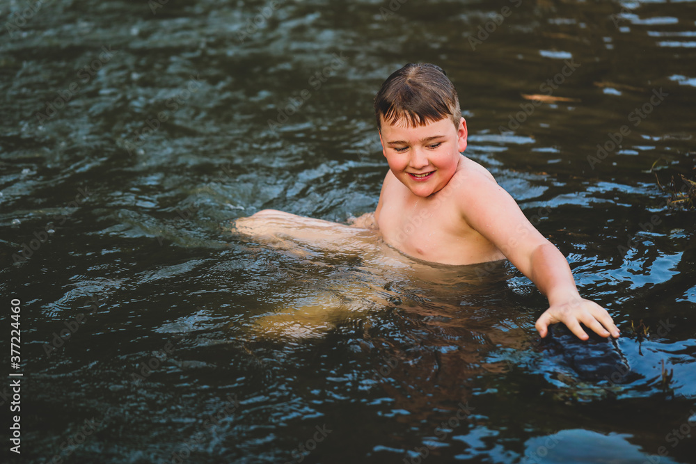 Fototapeta premium Boy swimming in river at dusk with big smile. Moody image with rich tones