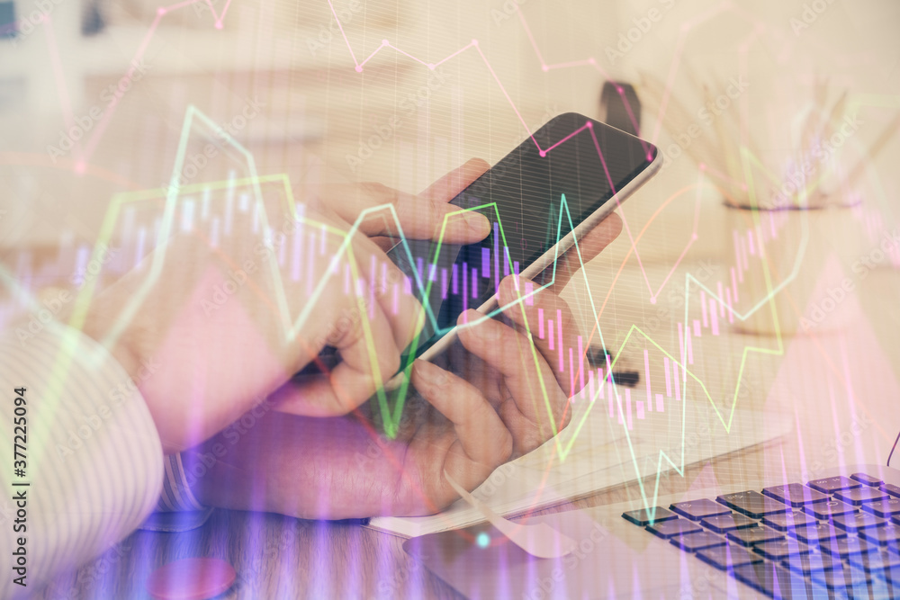 Double exposure of man's hands holding and using a digital device and forex graph drawing. Financial market concept.