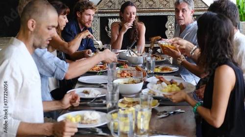 Diverse group of multiethnic friends enjoying meal sharing and passing food to each other in outdoor cafe or home. Leisure, food and drinks, people and holidays concept