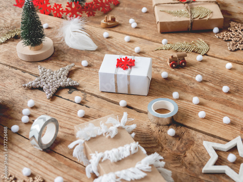 Christmas presents wrapped in craft paper with white fluffy pompons and fringe as decoration. Wooden table with hand made New Year gifts for children with toy ship and train.