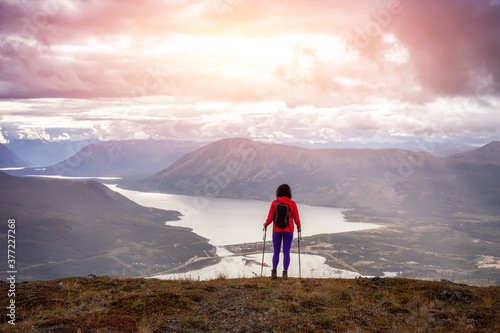 Adventurous Girl Hiking up the Nares Mountain during a cloudy and sunny evening. Taken at Carcross, near Whitehorse, Yukon, Canada. photo