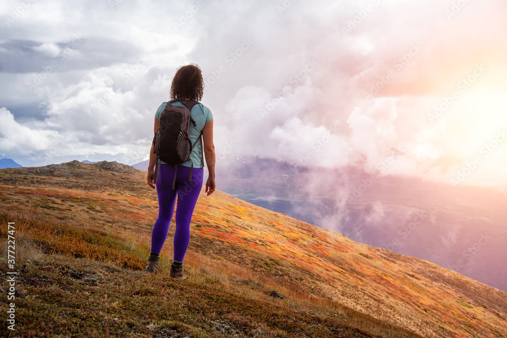 Adventurous Girl Hiking up the Nares Mountain during a cloudy and sunny evening. Taken at Carcross, near Whitehorse, Yukon, Canada.