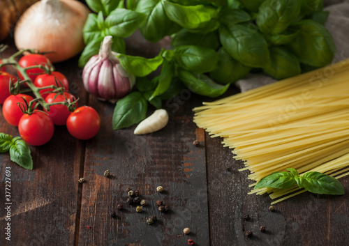 Raw spaghetti pasta in glass bowl with oil and garlic  basil and tomatoes with pepper and onion on wooden background