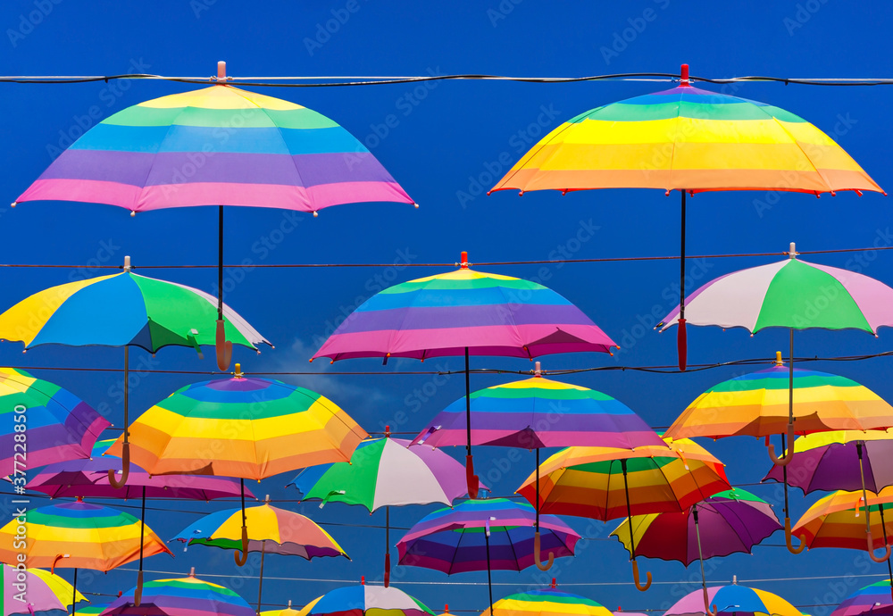 Rainbow Colored Umbrellas Hanging On The Background Of A Blue Sky