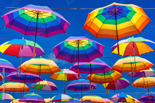 Rainbow Colored Umbrellas Hanging On The Background Of A Blue Sky