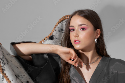 Fashion studio portrait of young teenage female model with long brunette straight hair and makeup with pink eye shadows in silver kimono. Closeup breast up portrait. photo