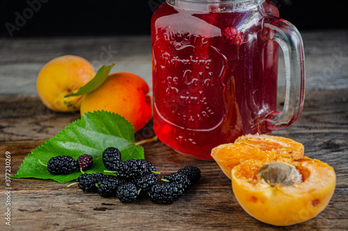 Homemade, rustic compote of apricot and mulberry in a glass with a straw on old wooden boards.