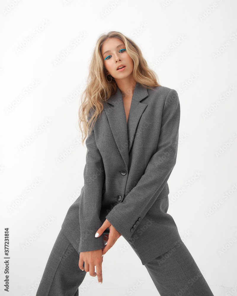 High fashion body length portrait of young beautiful female blonde model in classic gray male suit. Vogue style. Girl with blue eye arrows standing on white background High fashion body length portrait of young beautiful female blonde model in classic gray male suit. Vogue style. Girl with blue eye arrows standing on white background