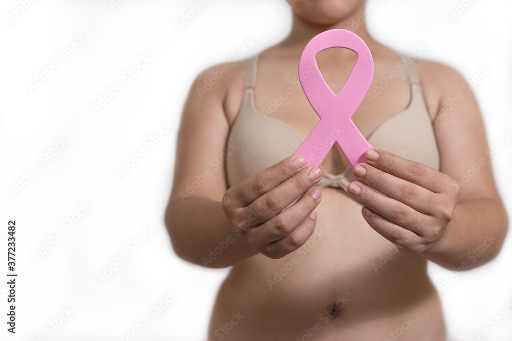Latin woman holding pink ribbon in bra with a white background to use in October breast cancer awareness month BCAM