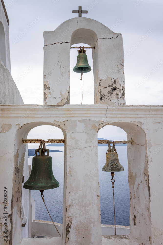 Obraz premium Close-up of a rustic old bell tower in Oia, Santorini island with mediterranean sea background on a cloudy day.