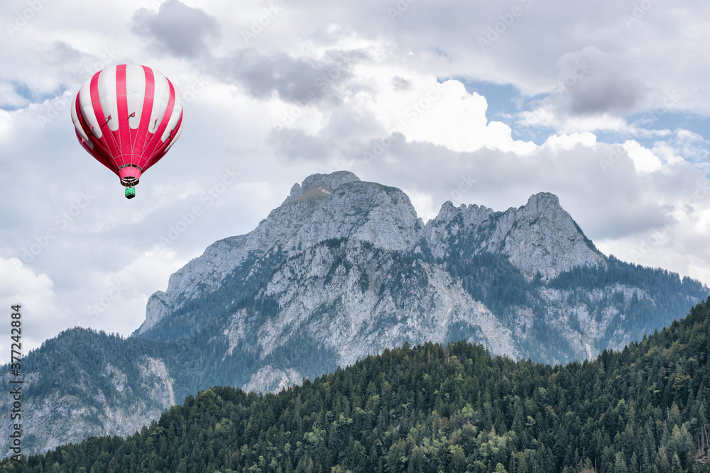A great view of the high Alps mountains wth green forest and a hot air balloon under blue cloudy sky.