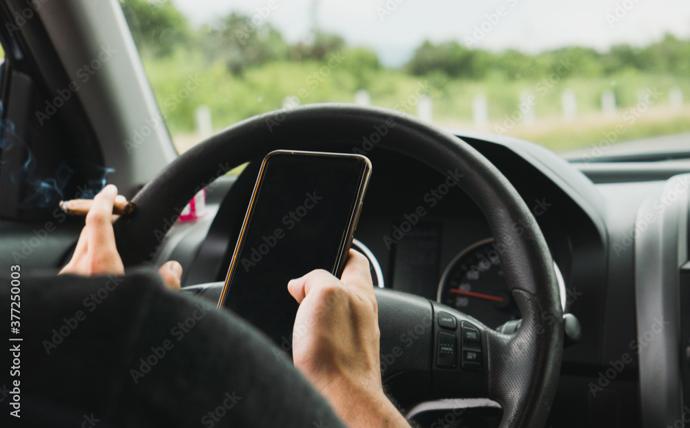 young man smokes joint of marijuana cannabis while driving and looking at his cell phone