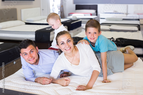 Man with woman and children are testing quality of mattress in store.