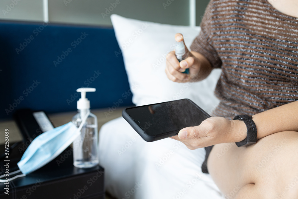 Fototapeta premium Hands of asian woman clean the phone with medical alcohol,disinfectant spray, cleaning spraying on mobile phone to kill germs,safety from the Coronavirus,new normal life condition under the COVID-19