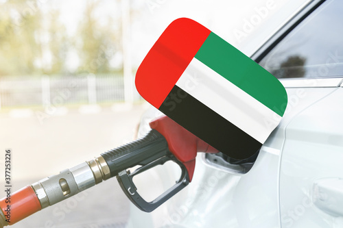 Flag of United Arab Emirates on the car's fuel filler flap with gas pump nozzle in the tank.