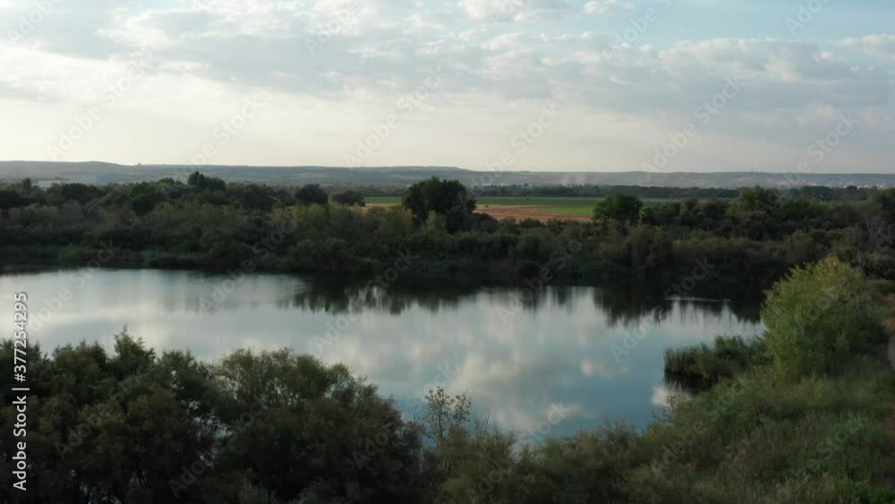 Drone shot of lake with clouds reflected on water and lakeside forest. Aerial shot. Drone shot of lake with clouds reflected on water and lakeside forest. Aerial shot.