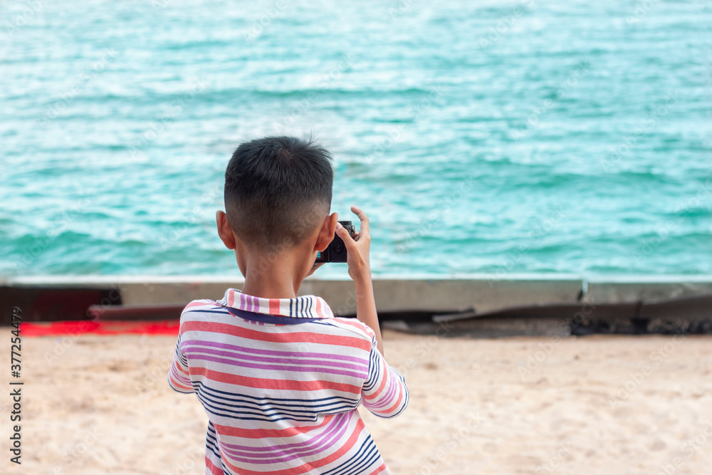 Asian boy stand to take pictures of the sea while traveling on holiday.