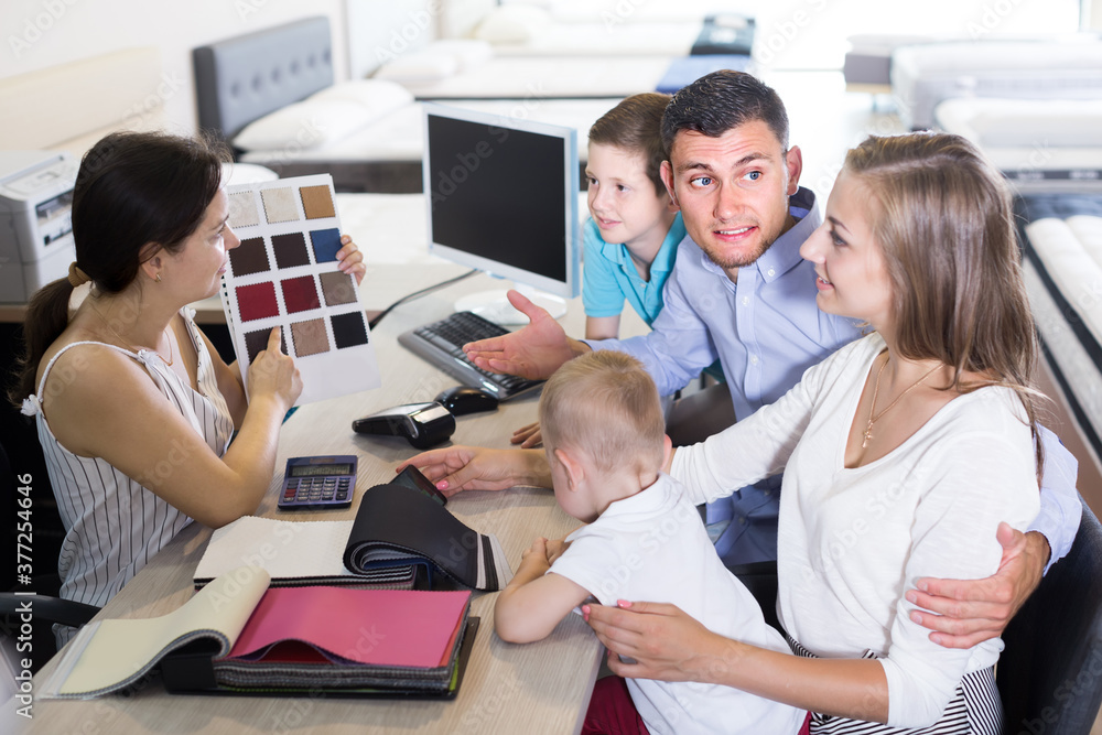 Fototapeta premium Positive saleswoman in furniture store helping young family in choice of mattress material