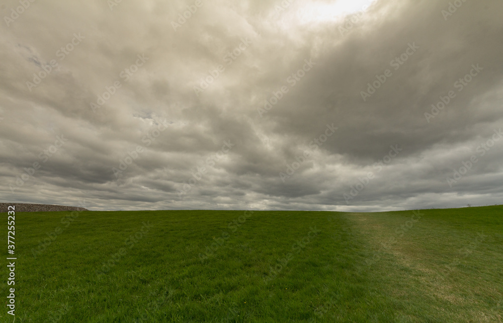 Fototapeta premium Dark stormy clouds over a green grass field
