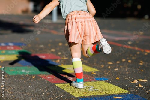 Closeup of leggs of little toddler girl playing hopscotch game drawn with colorful chalks on asphalt. Little active child jumping on playground outdoors on a sunny day. Summer activities for children. photo