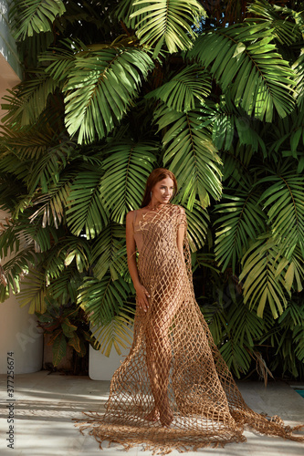 Beautiful, gorgeous young woman with slim tanned body in stylish bikini is posing near the wall of green foliage and leaves in the park, tropical vacation photo