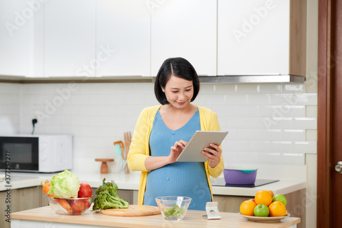 pregnant woman on kitchen making healthy salad with digital tablet