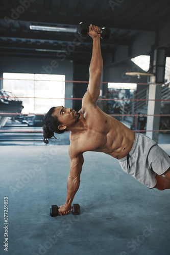 Workout. Man With Dumbbells Doing Side Plank On Boxing Ring. Shirtless Asian Sportsman Training At Gym. Topless Sexy Guy With Strong, Healthy Muscular Body Using Fitness Equipment For Bodybuilding.