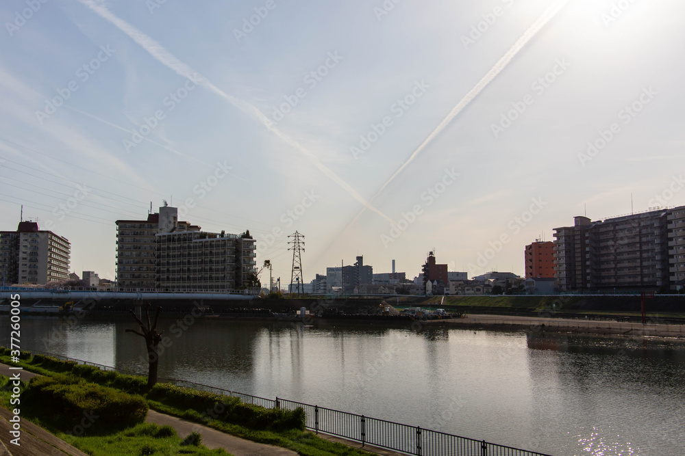 Obraz premium 都市の河川と飛行機雲が交差している空