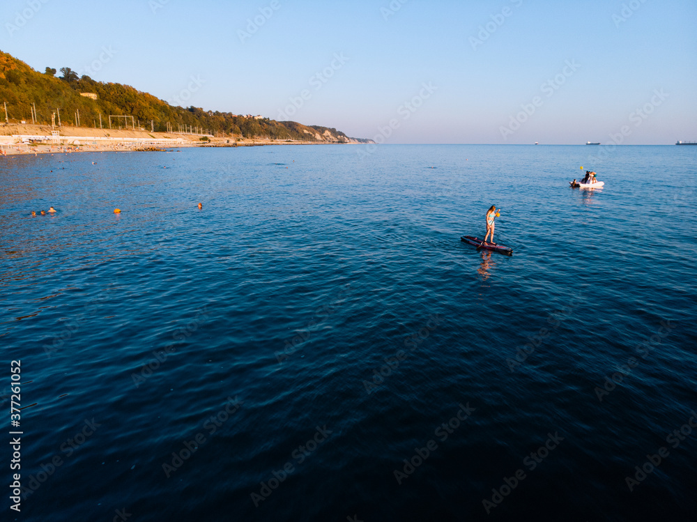 Attractive Woman on Stand Up Paddle Board, Woman paddling on sup board and enjoying turquoise transparent water. Tropical travel, wanderlust and water activity concept. Sunset and relax